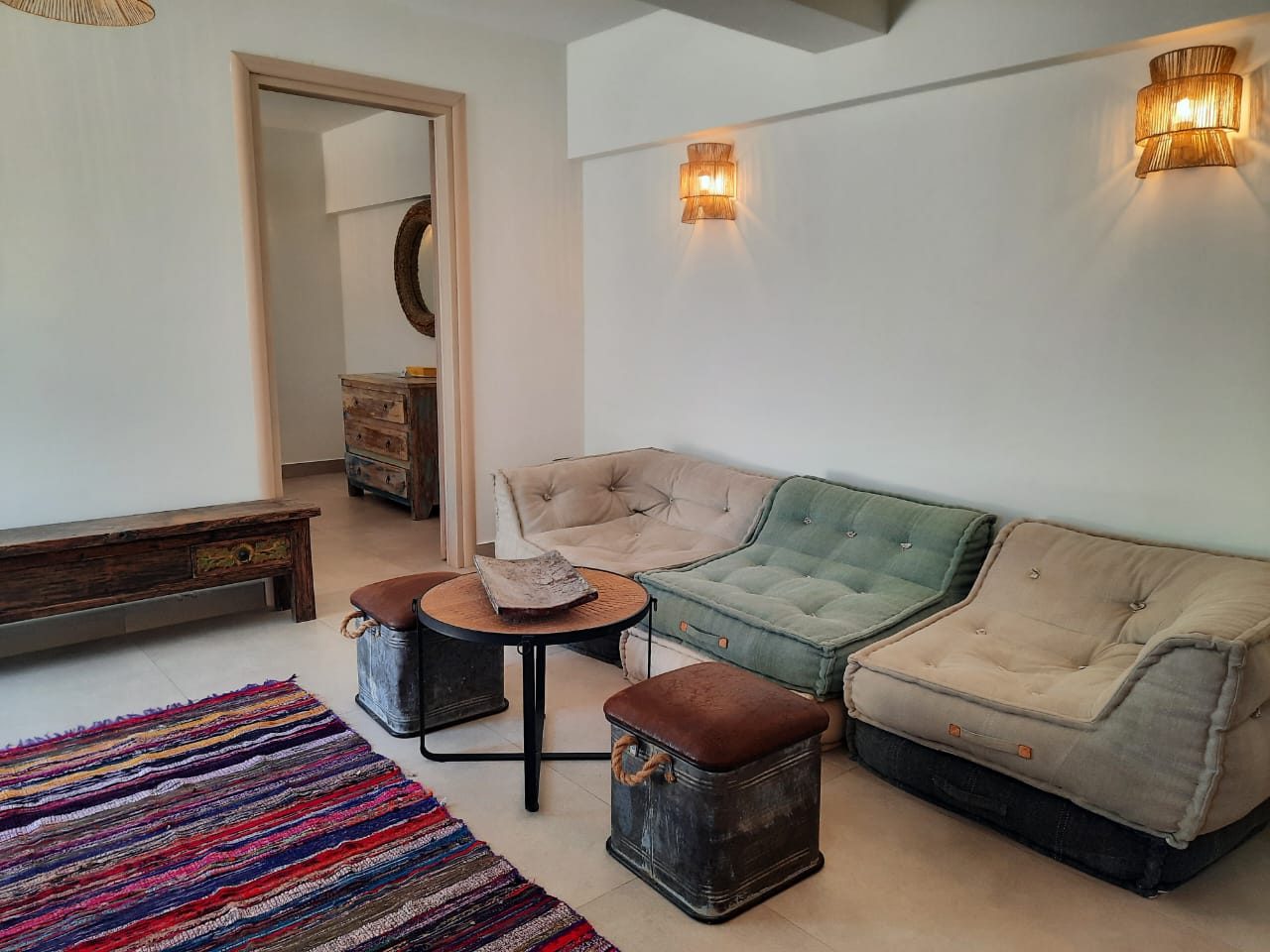 Sitting area in the Mistral studio with low cushioned sofas, rattan lights and a woven rug